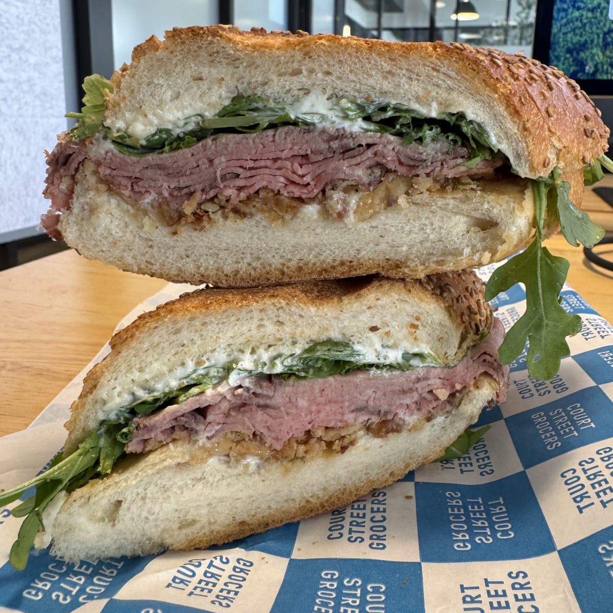 A cut sandwich with roast beef, french's fried onions, horseradish mayo, and arugula on a seeded hero.
