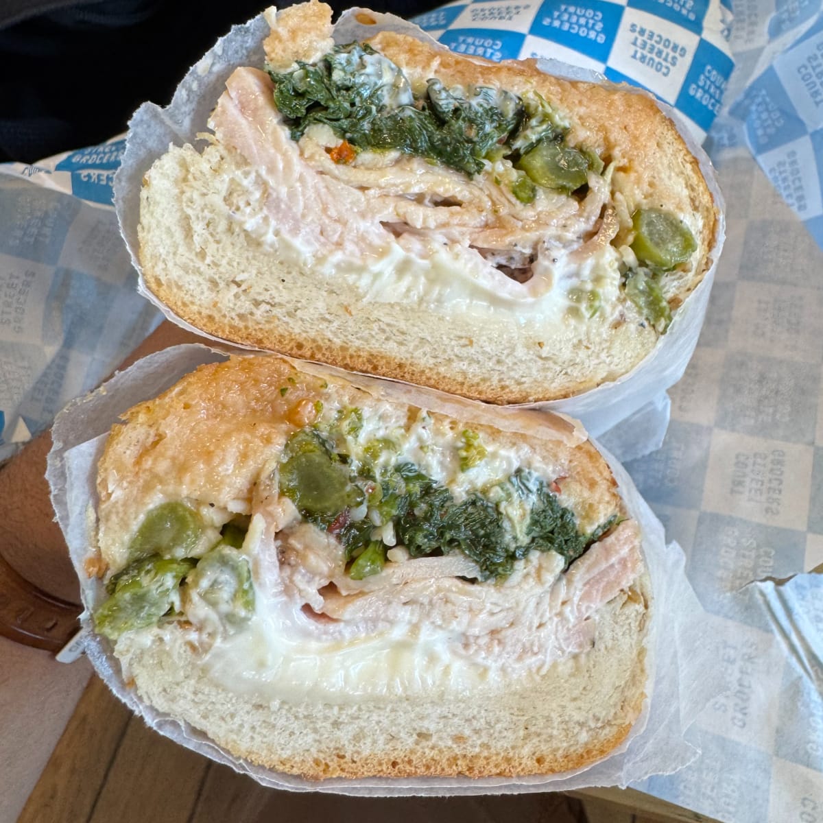 A cut sandwich with roast turkey breast, provolone, broccoli rabe, crystal hot honey, and mayo on a seeded hero.